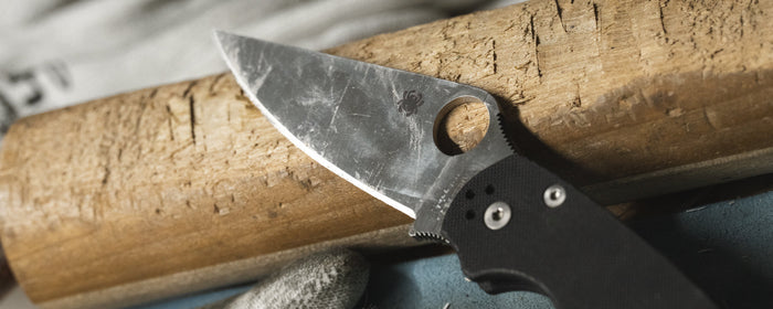 A dirty knife blade resting on a rough piece of wood.