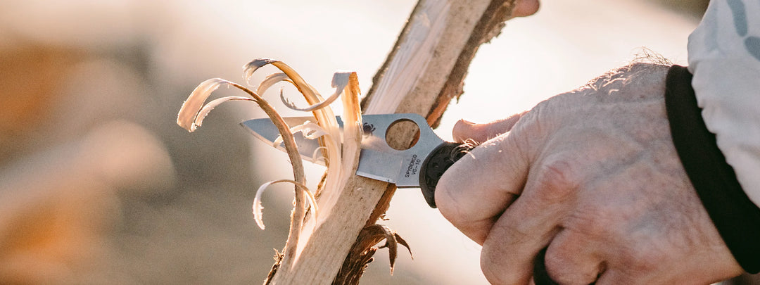 An image of a Spyderco folding knife being used to make feather sticks from a piece of wood.
