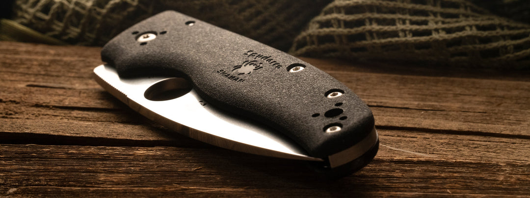 The Spyderco Shaman pocket knife sitting on rough wood.