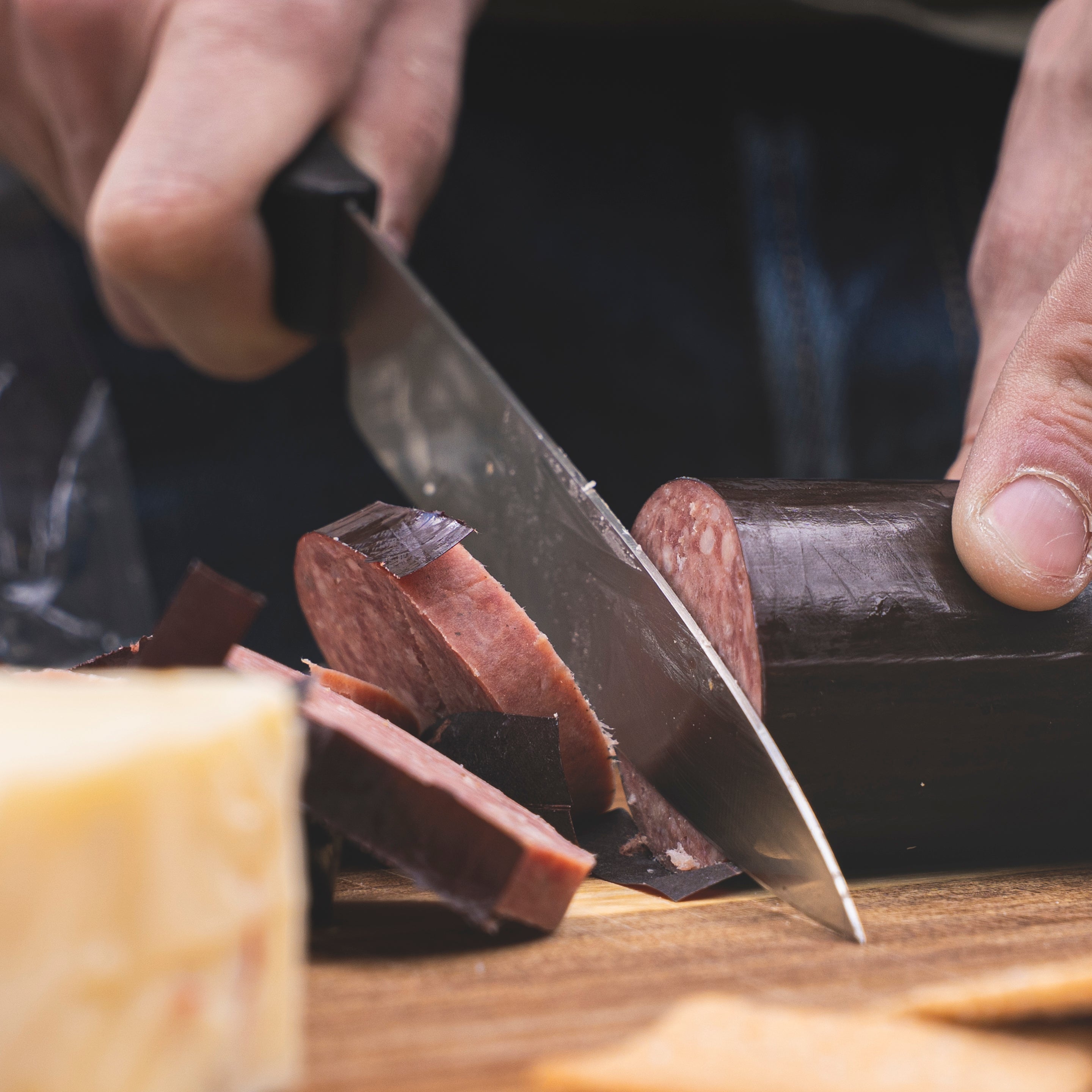 A Spyderco Kitchen knife cutting summer sausage outdoors on a cutting board. 