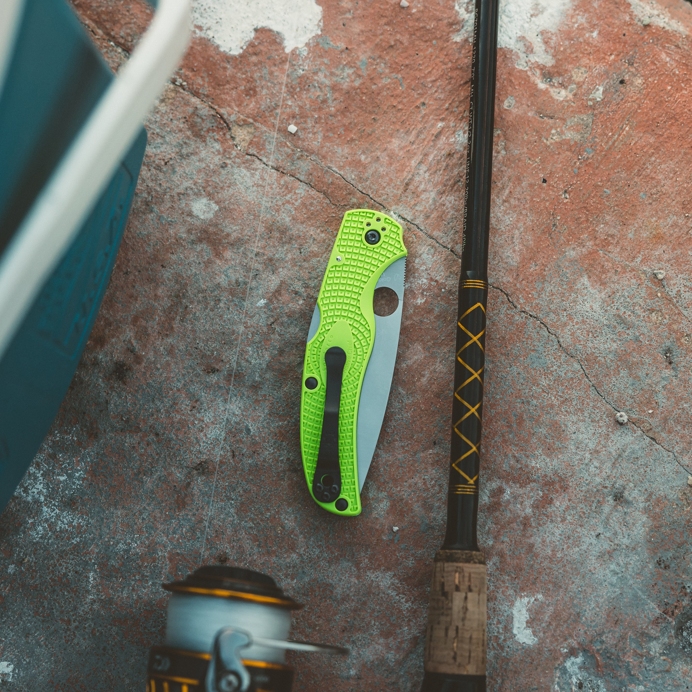 A closed green Spyderco Native Chief sits closed alongside a fishing pole and cooler
