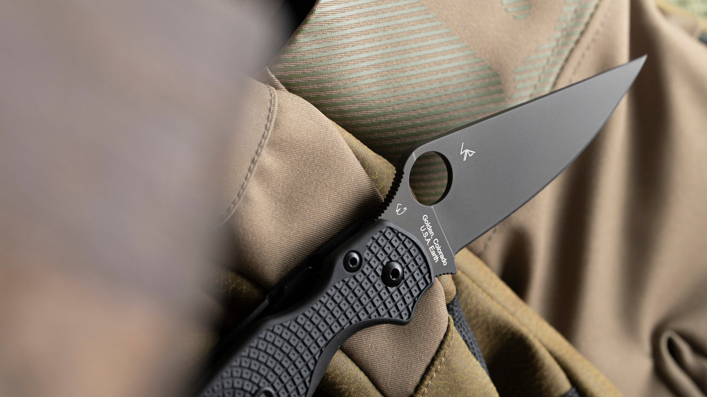 Para Military 2 Lightweight with an all black blade resting on a pair of gloves. Shown is the designer tags of Eric and Sal Glessar with the origins of the knife "Golden, Colorado U.S.A., Earth" on. the base of the blade.